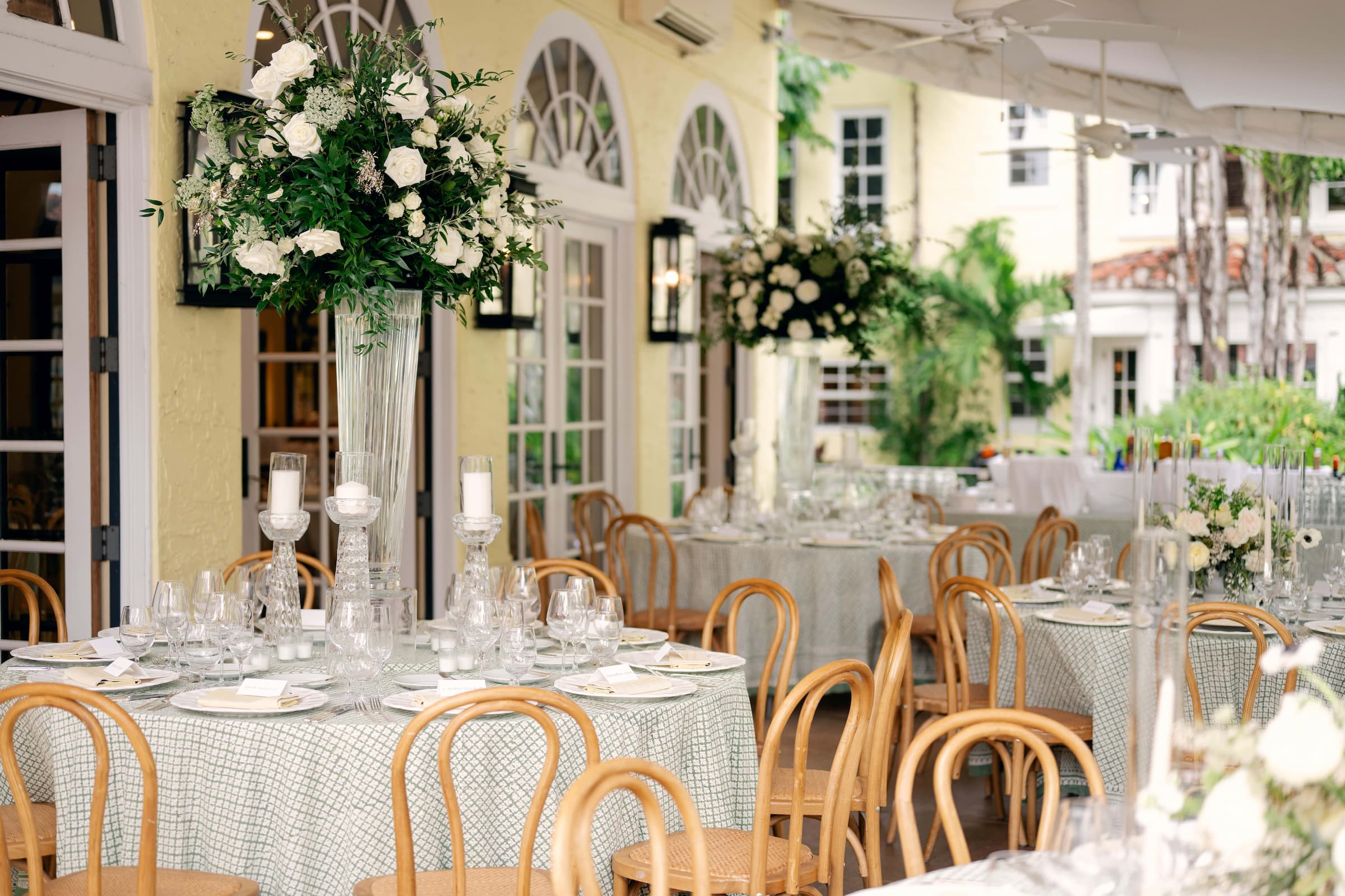 Round tables in a green lattice block print beneath tall white florals, Palm Beach