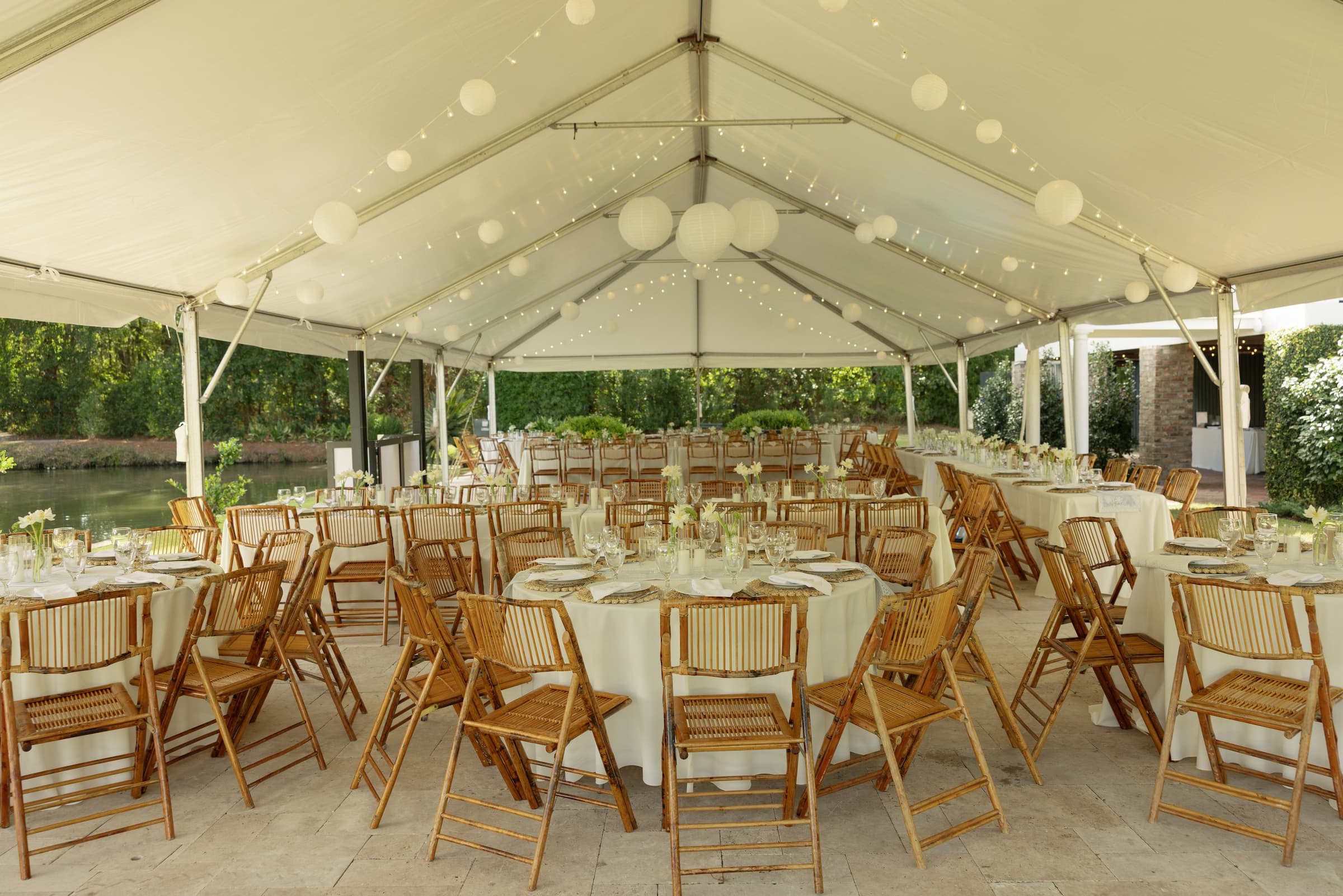Tented reception beside the water set with bamboo chairs and long tables