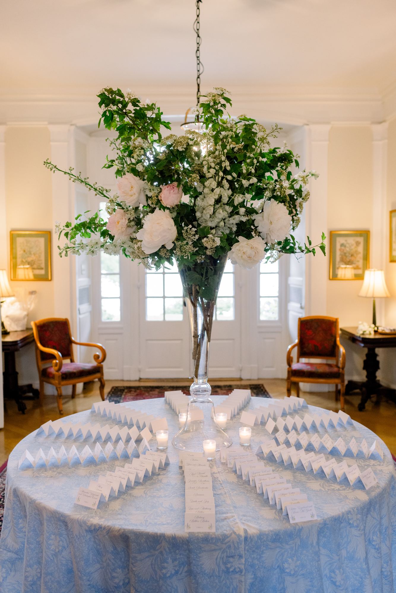 Escort card table in a blue block-printed cloth beneath a tall white arrangement