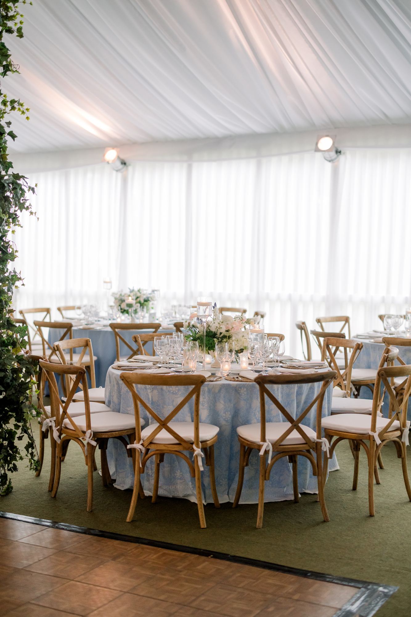 Round tables in a pale blue block print with cross-back chairs under a draped tent