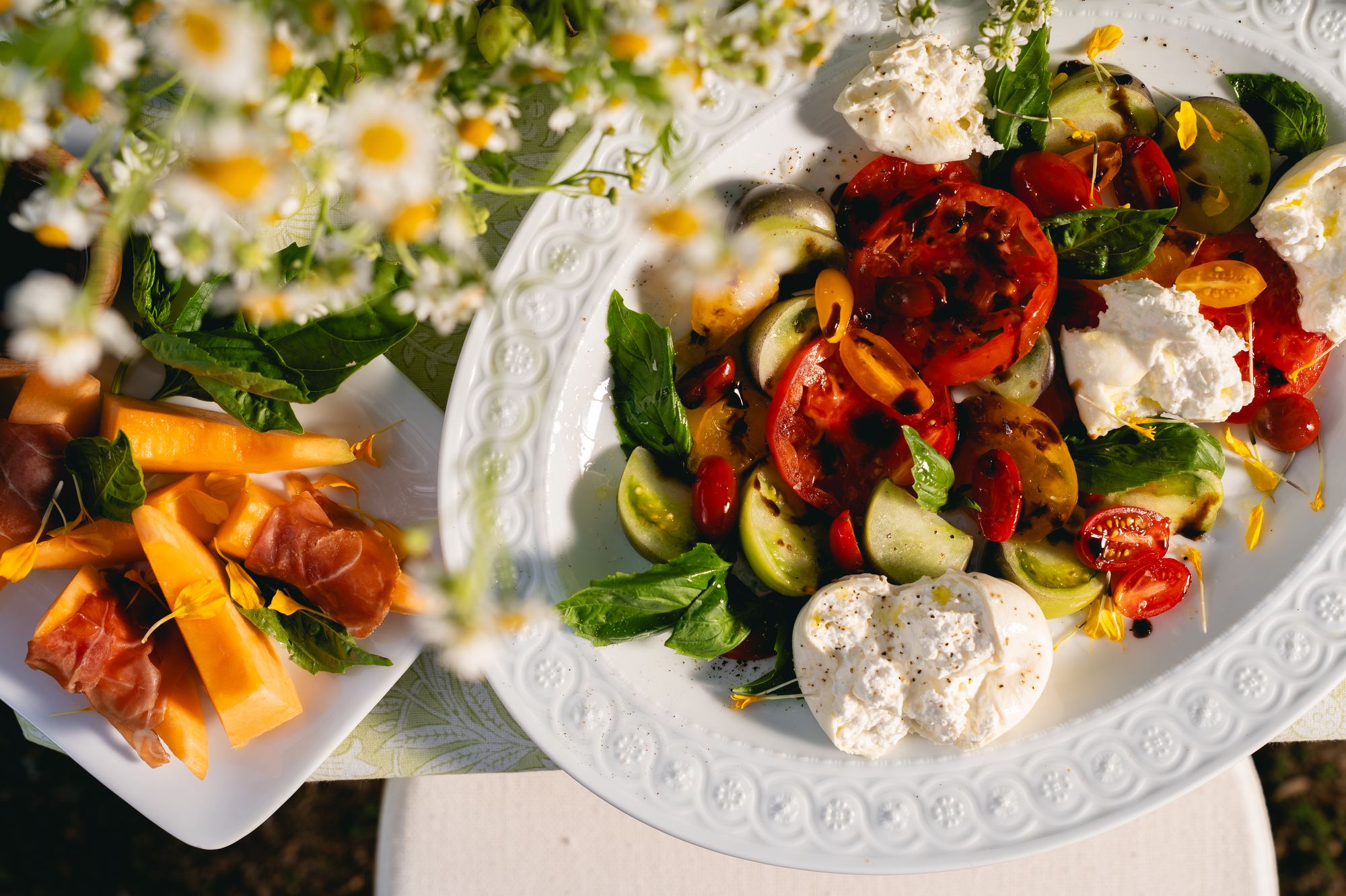 Overhead platters of heirloom tomatoes and burrata on a printed cloth